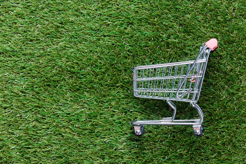 Self-service supermarket shopping trolley cart on spring or summer green grass lawn background